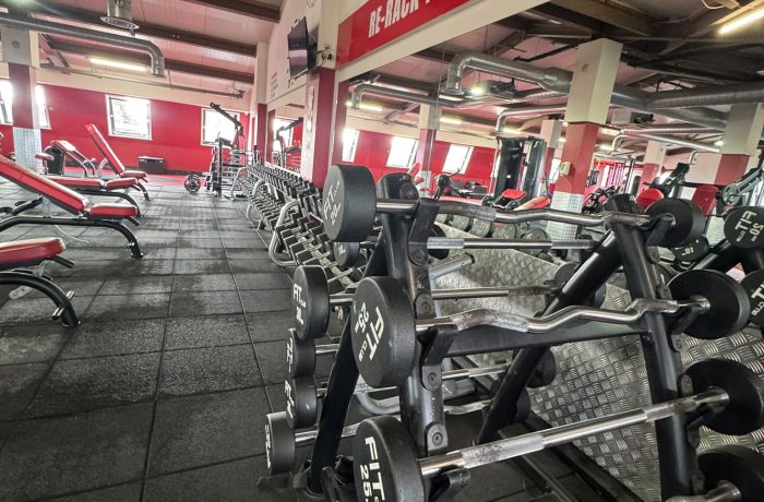 Fixed-weight barbells and EZ curl bars beside the mirrored free weights area at Fit Club Northwood Hills